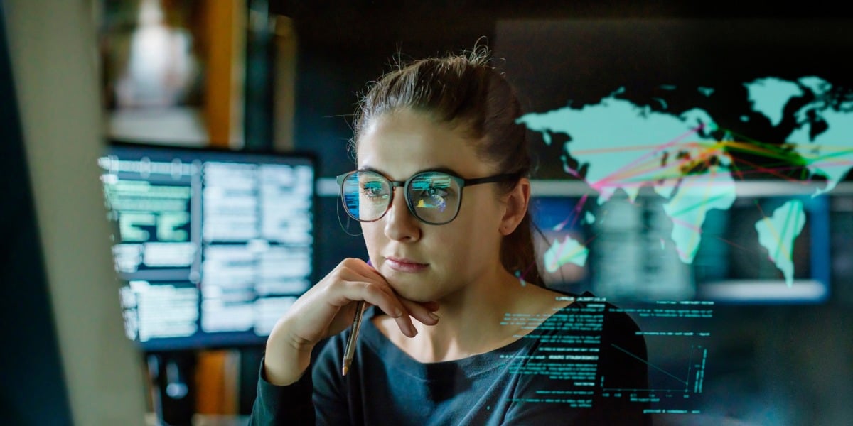Woman with glasses on analysing data across multiple computer screens